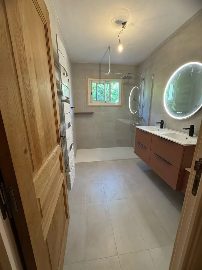 Salle de bains rénovée vue depuis une porte en chêne, avec douche à l'italienne vitrée et meuble double vasque