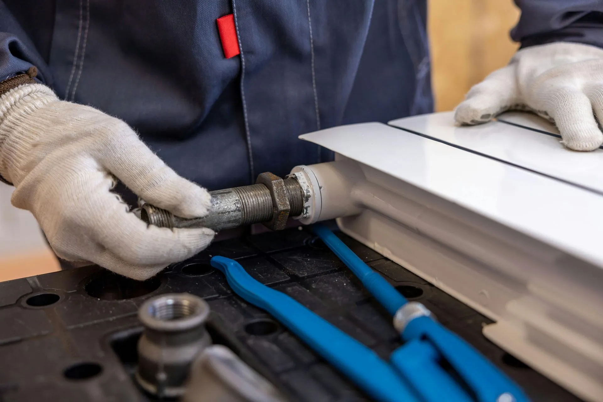 Mains gantées d'un plombier en bleu de travail vissant un raccord fileté