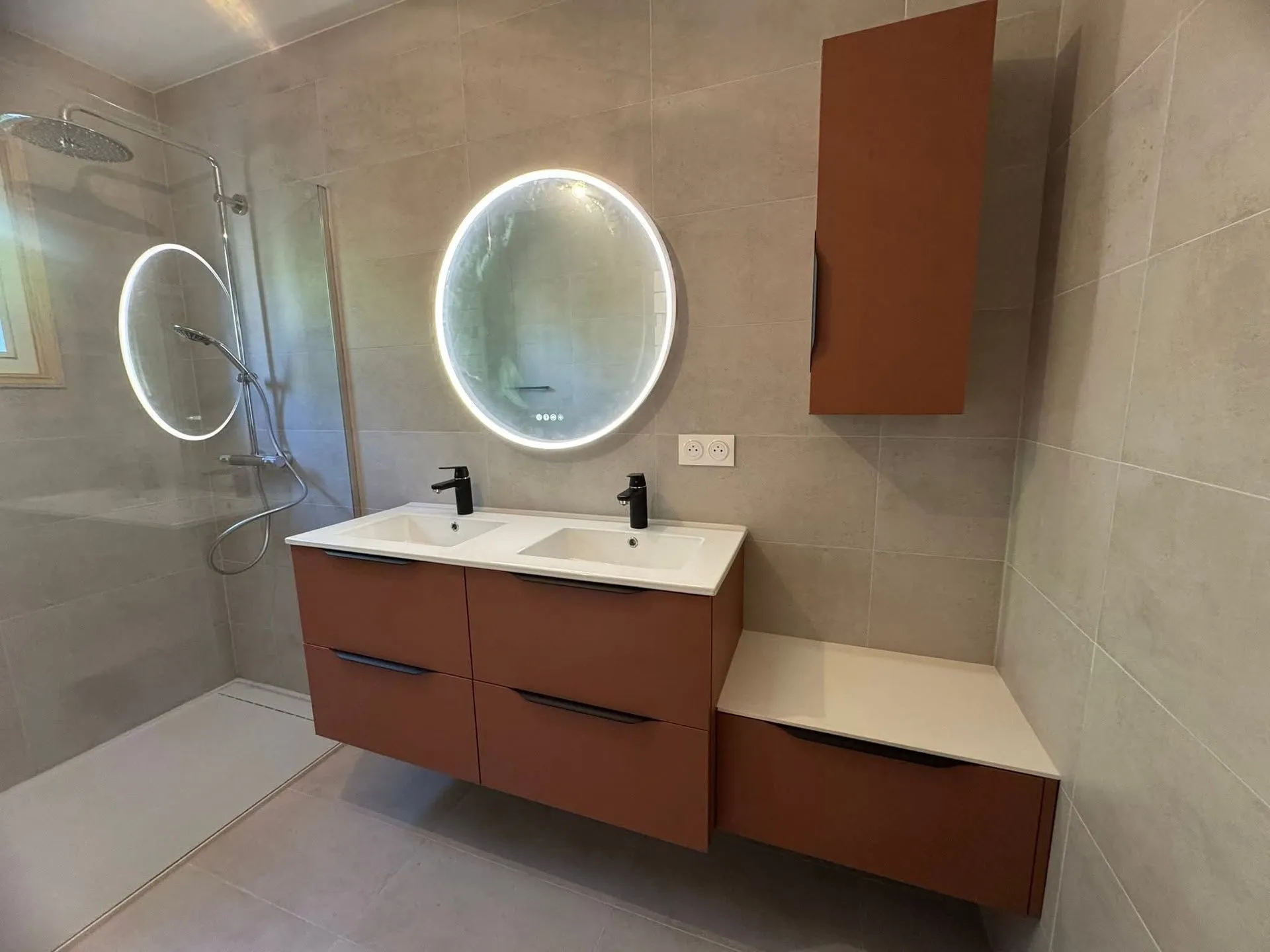 Salle de bains rénovée avec meuble suspendu terracotta à double vasque blanche et miroirs ronds rétroéclairés