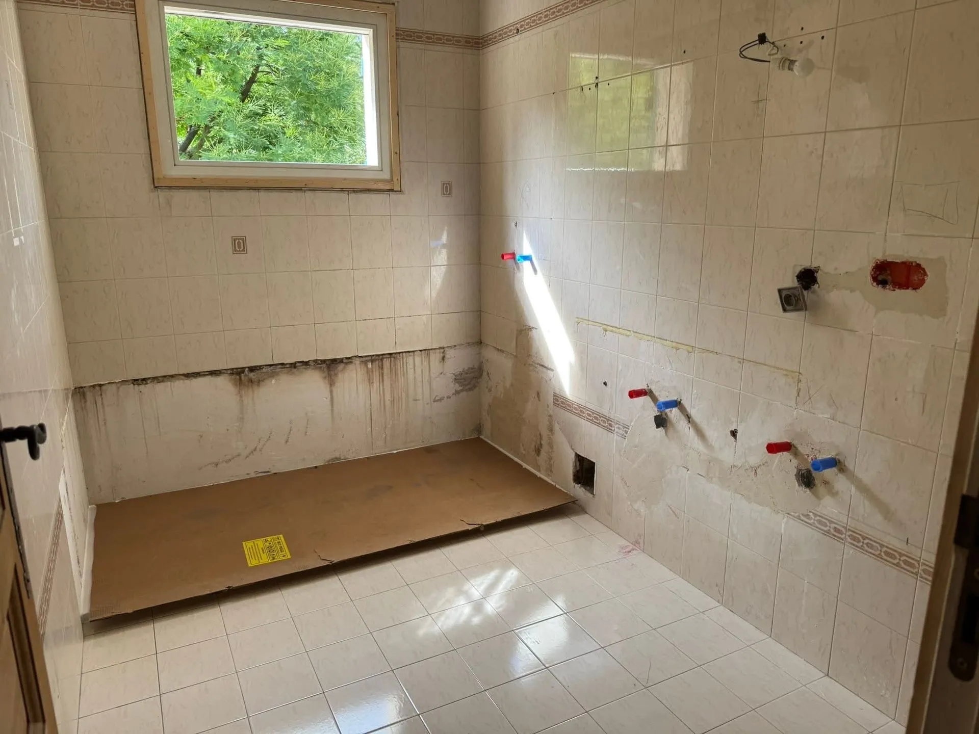 Salle de bains en cours de démolition, carrelage mural partiellement déposé et arrivées d'eau apparentes