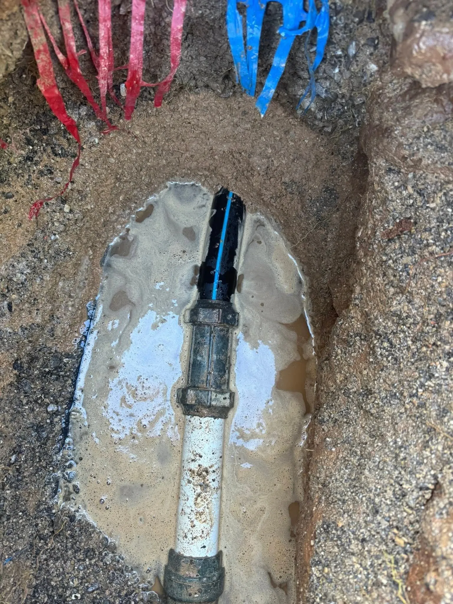 Tranchée inondée où un tuyau polyéthylène noir à liseré bleu est raccordé après réparation