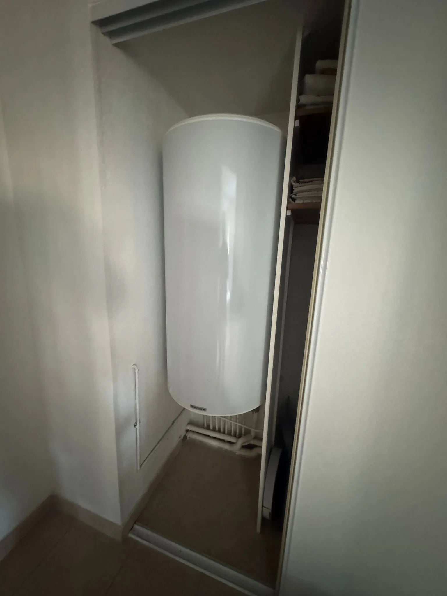 Chauffe-eau électrique vertical blanc installé dans un placard encastré à porte coulissante