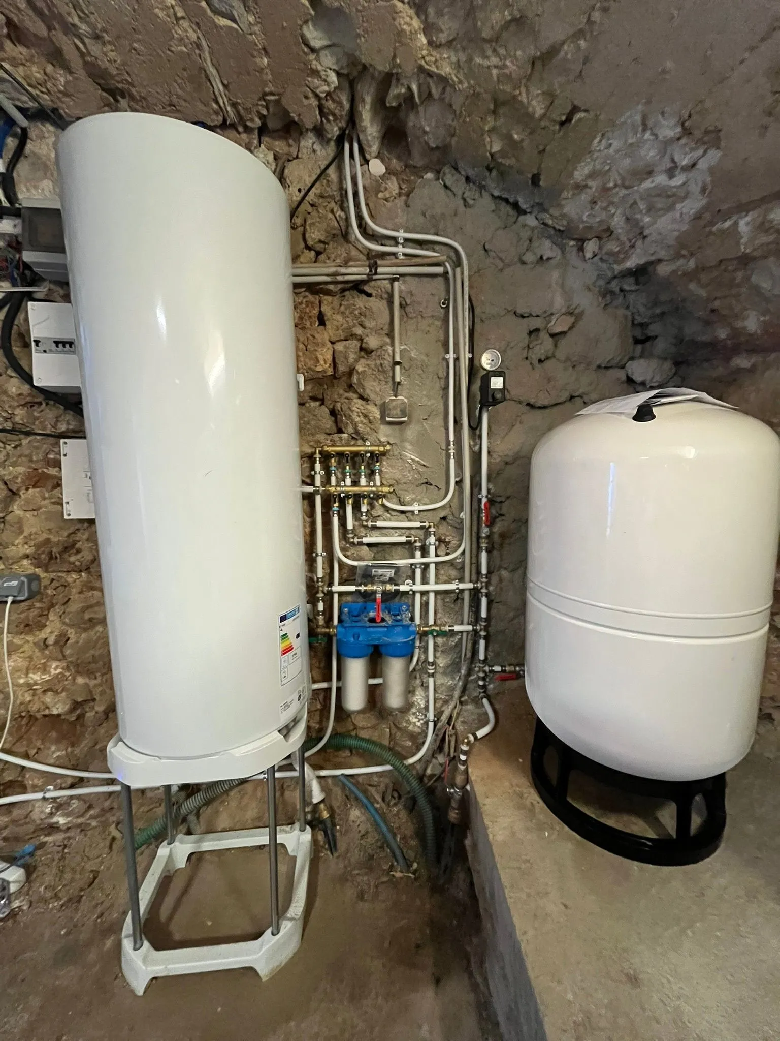 Local technique en pierre apparente avec un grand chauffe-eau vertical blanc et un collecteur en laiton