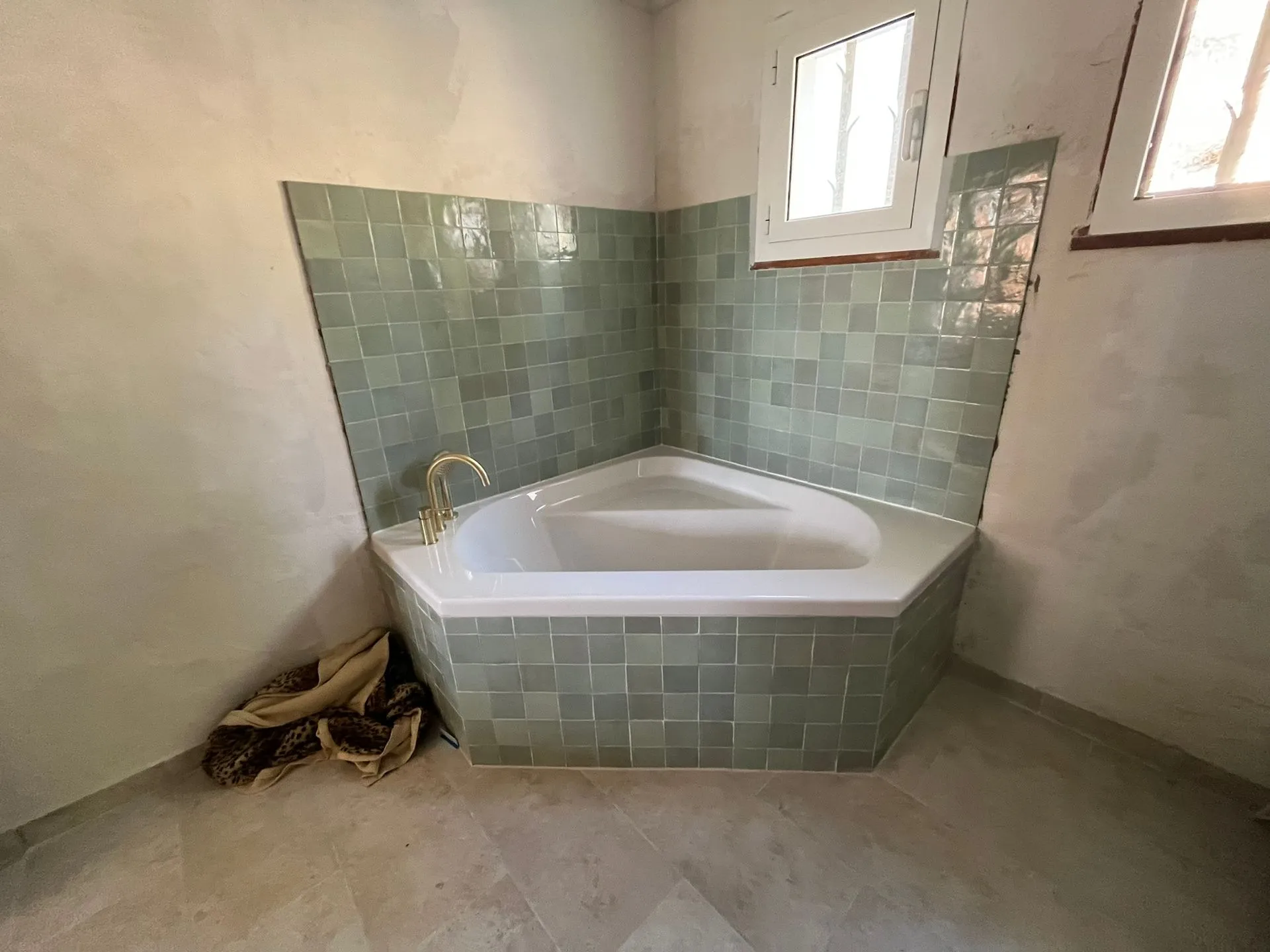 Baignoire d'angle blanche avec robinetterie dorée, murs habillés de zelliges vert d'eau