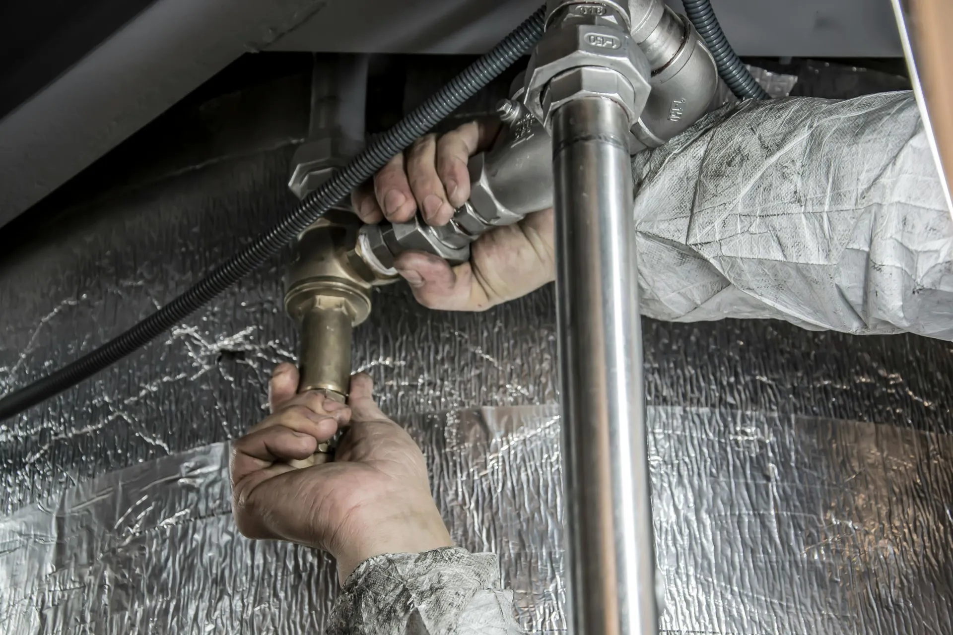 Mains d'un plombier serrant un raccord en laiton sur des tuyaux inox