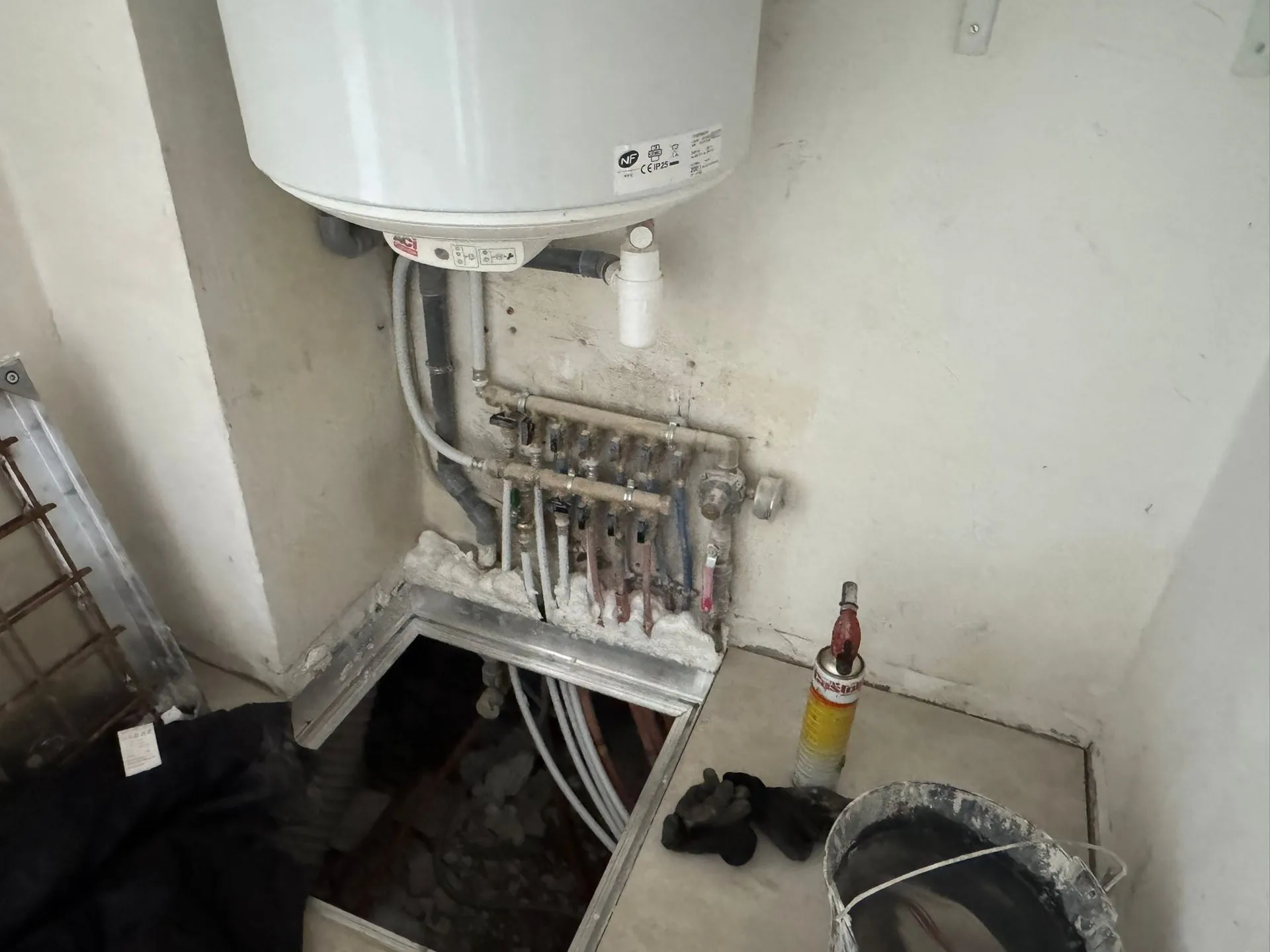 Chauffe-eau électrique vertical blanc fixé au mur au-dessus d'un collecteur de plomberie en laiton